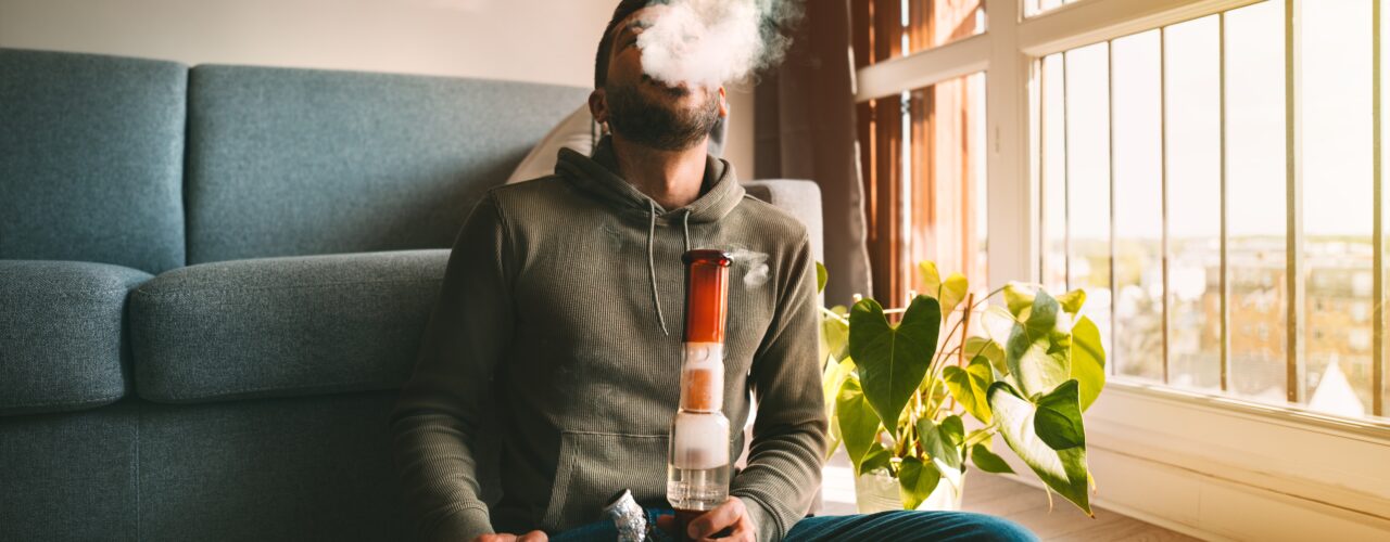 An image of a man smoking weed in an apartment.