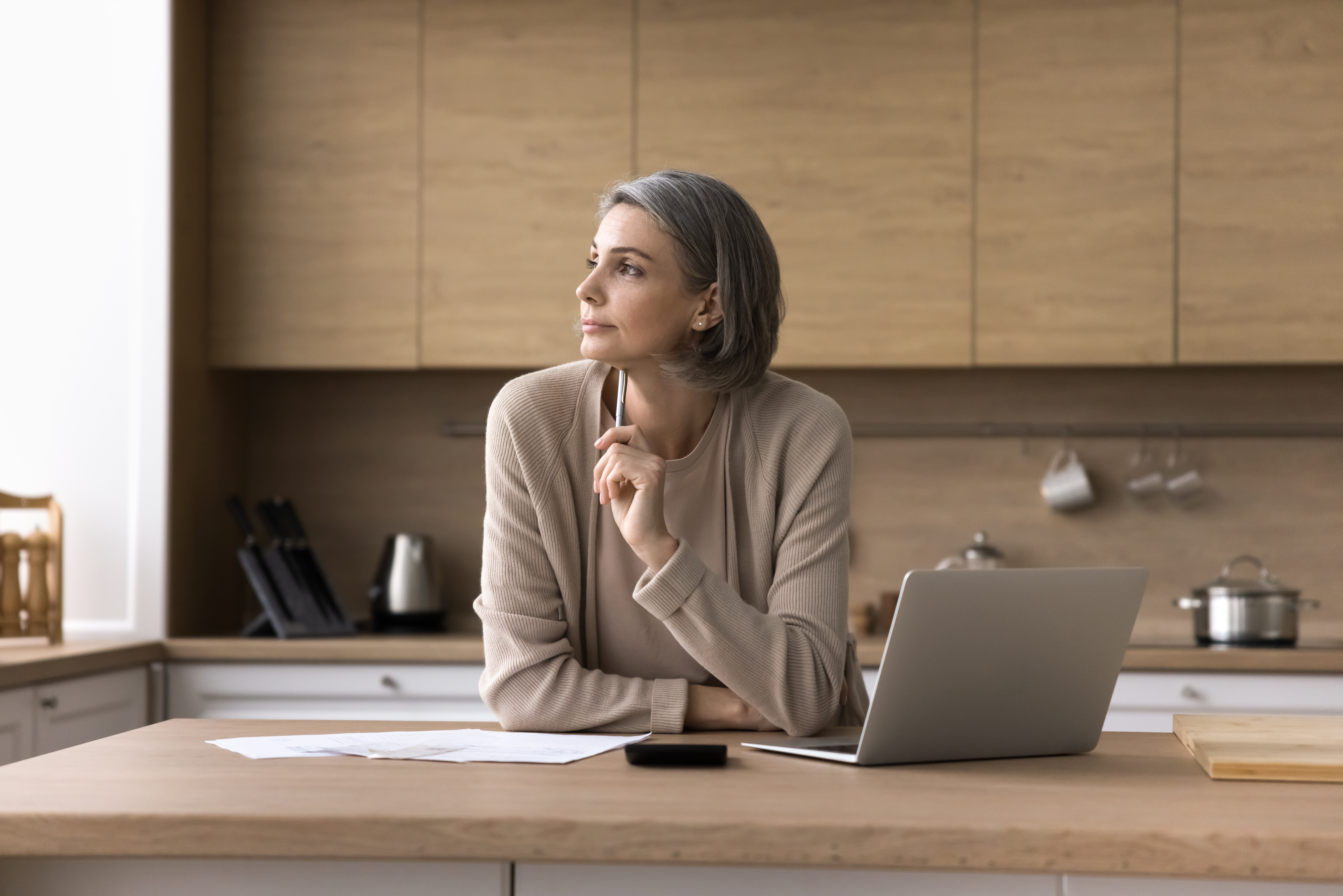 An elderly woman staring out the window with her laptop next to her