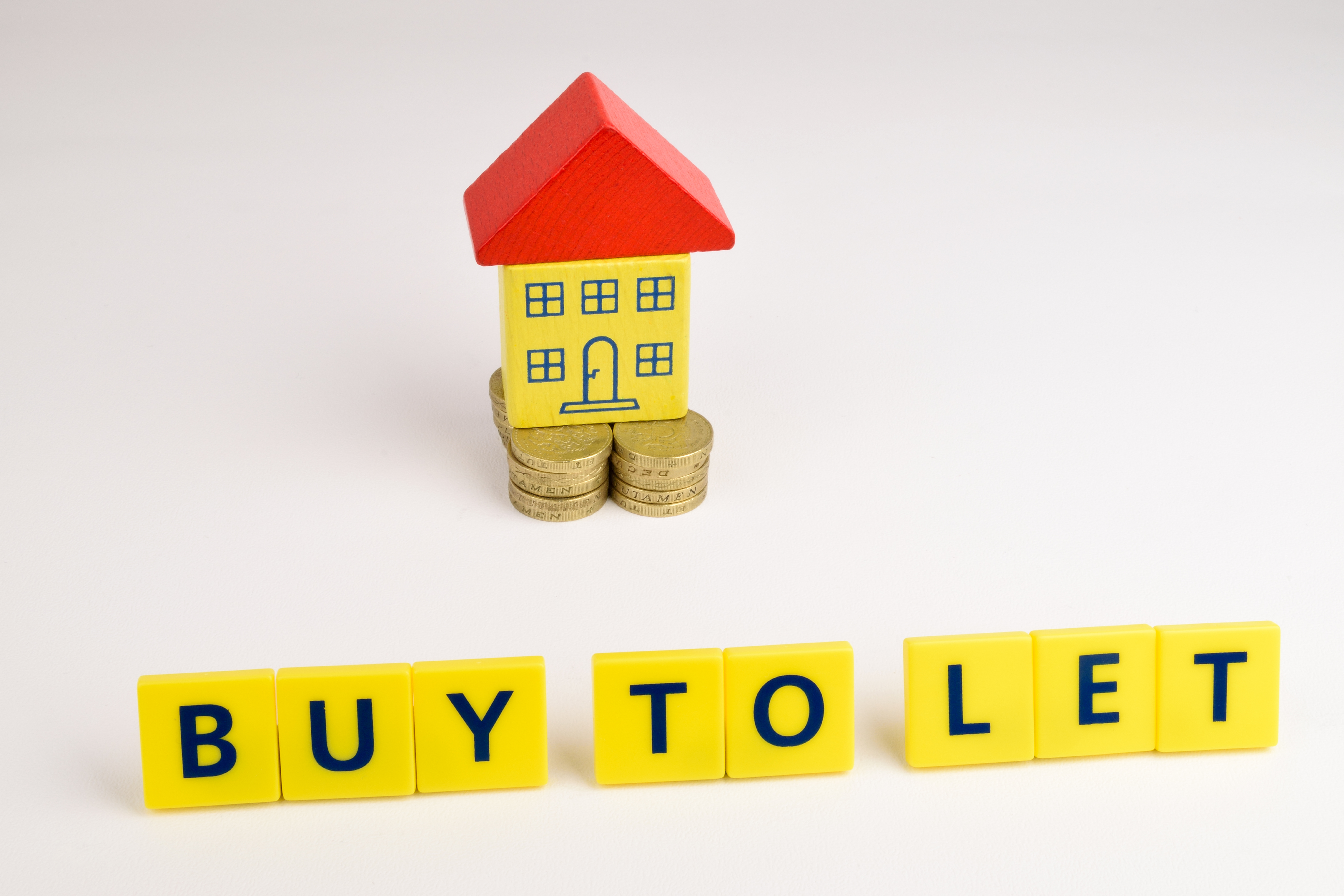 A model house on top of coins with a 'buy to let' sign in front of it 
